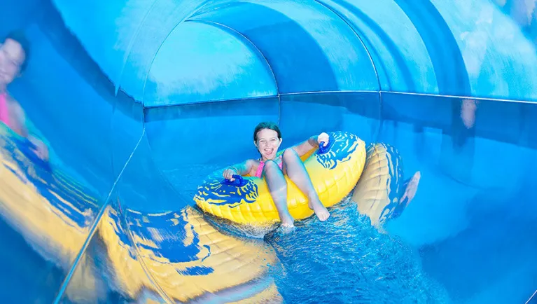 A girl smiles at the camera as she rides a tube down a water slide at a Great Wolf Lodge indoor water park.